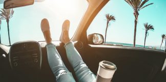 Girl relaxing in auto trip reading travel book with ocean beach and palms in background - Focus on hands