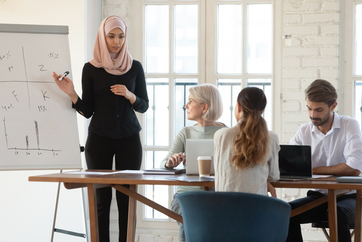 millennial female Arabic speaker explaining presentation to older and young colleagues at office.