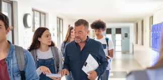 High school student asking doubt to professor while walking in hallway. Mature man professor answering to girl in university campus. High school lecturer talking to schoolgirl at the end of the lesson while walking in the corridor.