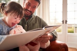 Father With Down Syndrome Daughter Reading Book At Home Together